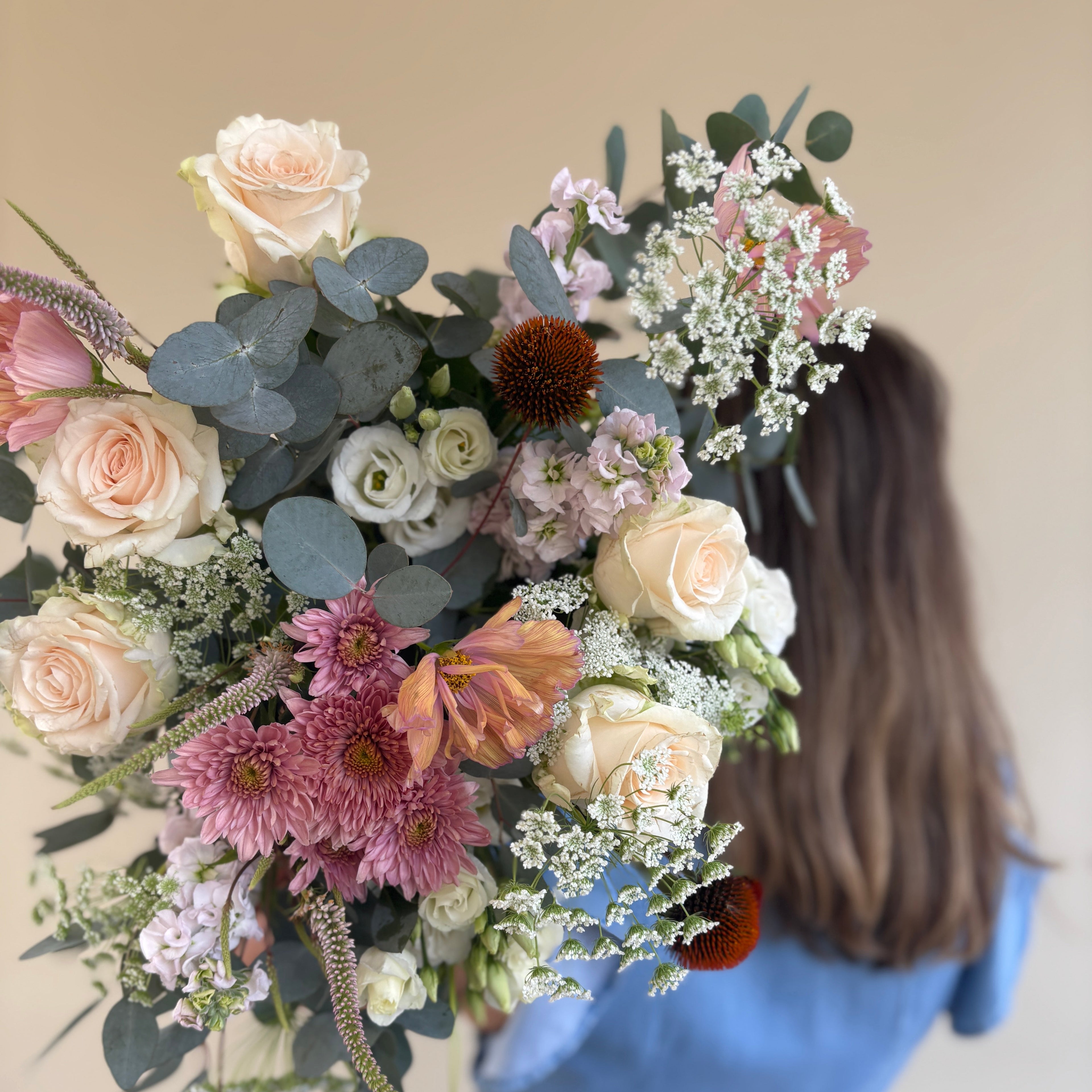 Person holding a large, colorful bouquet of flowers against a neutral background