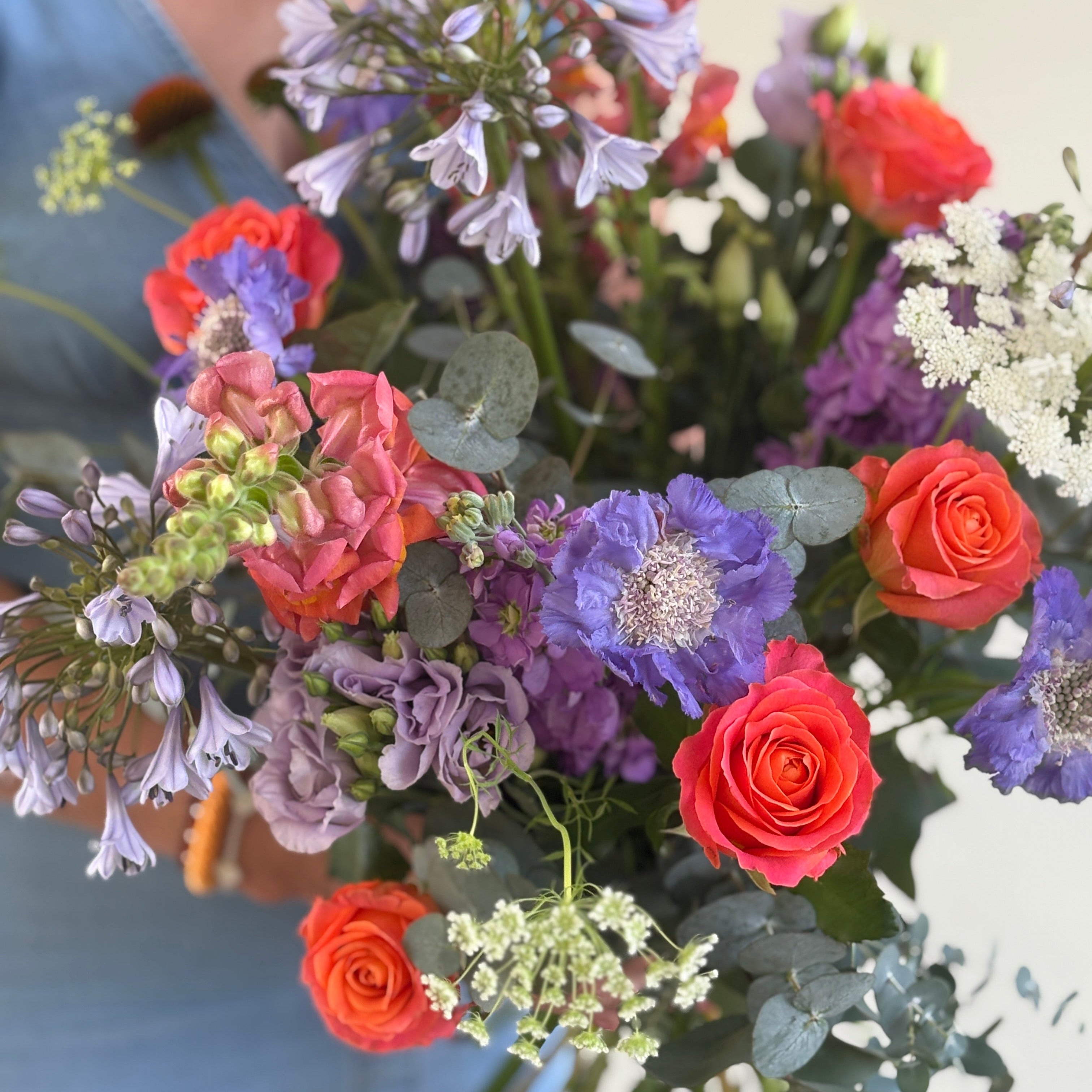 Bouquet of colorful flowers held by a person wearing a blue shirt.