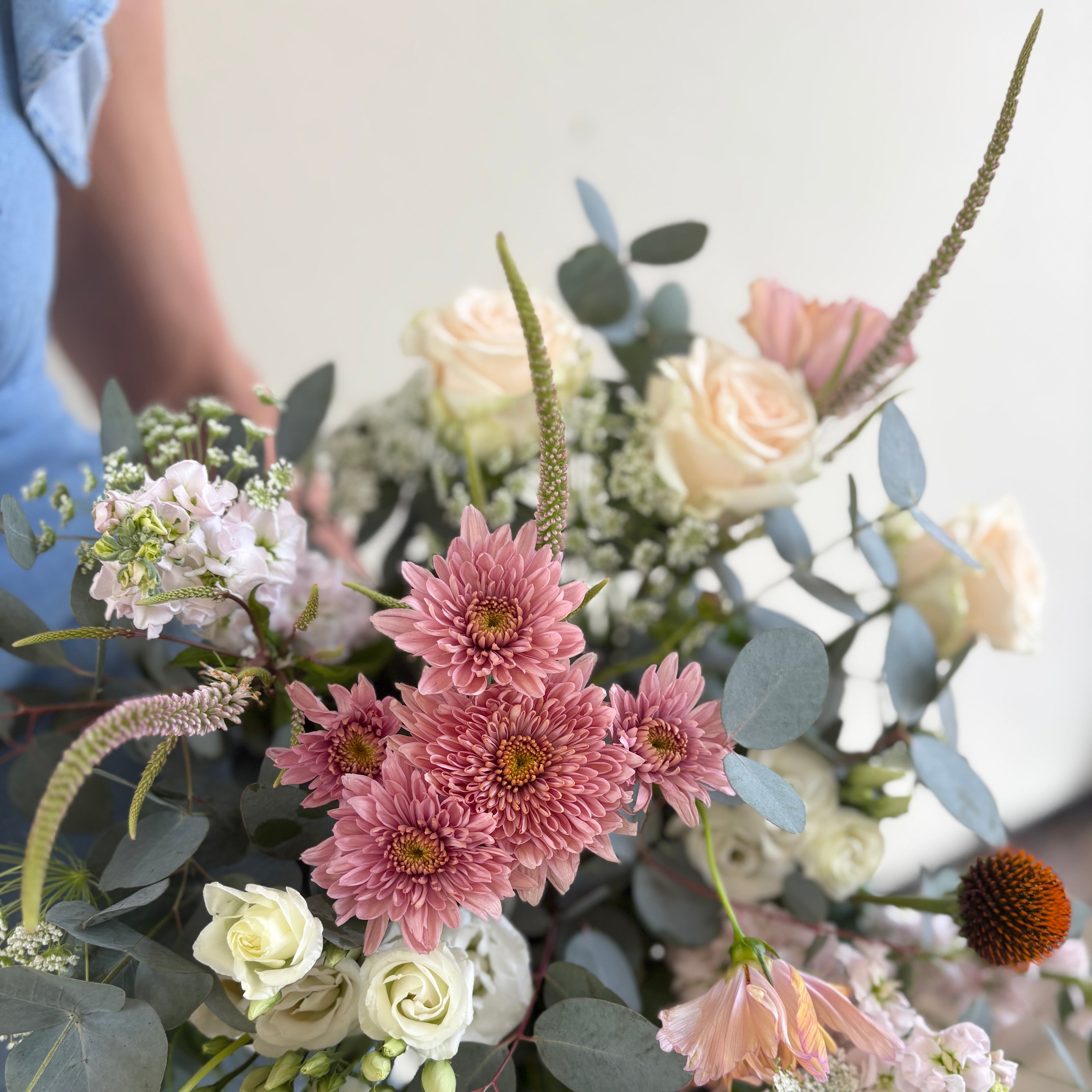 Bouquet of pink, white, and green flowers with a blurred person in a blue shirt in the background.